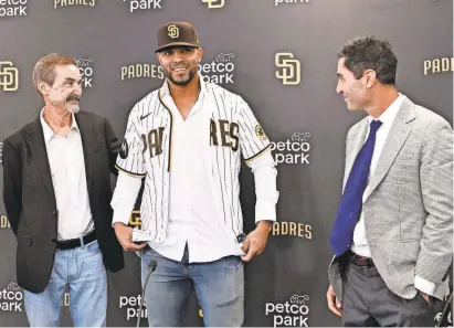  ?? /DENIS POROY/AP ?? Xander Bogaerts puts on his new team jersey as Padres general manager A.J. Preller, right, and team chairman Peter Seidler look on at a news conference Dec. 9 in San Diego.