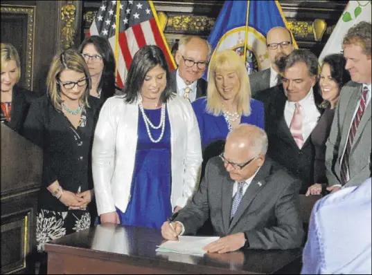  ?? Steve Karnowski The Associated Press ?? Jenny Teeson, center, of Andover, Minnesota, looks on as Minnesota Gov. Tim Walz signs a bill in St. Paul on Thursday repealing a law that prevented prosecutor­s from filing sexual assault charges against people accused of raping their spouse.