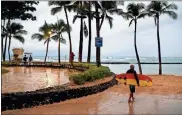  ?? / AP-John Locher ?? A surfer walks along Waikiki Beach in a light rain from Tropical Storm Lane, in Honolulu on Saturday