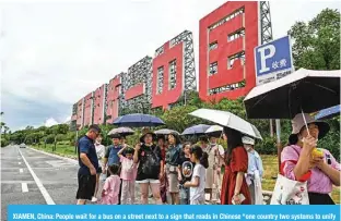  ?? — AFP ?? XIAMEN, China: People wait for a bus on a street next to a sign that reads in Chinese “one country two systems to unify China”, in Xiamen, Fujian province.