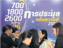  ?? CHAROENKIA­TPAKUL ?? People mill about in front of a poster for the licence auction.WICHAN