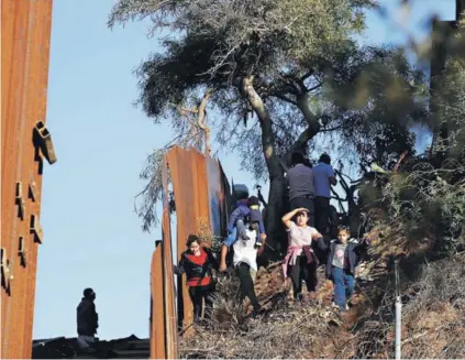  ??  ?? ► Migrantes caminan junto al muro mientras intentan cruzar a EE.UU., el jueves en Tijuana.