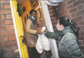  ??  ?? Volunteer Maria Martinez (right) hands bags of West Indian meals to Bridgette Toussaint prepared by members of the Preston Windrush Covid Response team in Preston, England.