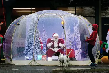  ?? (AP Photo/Ted S. Warren, File) ?? TOP RIGHT
Santa Claus, portrayed by Dan Kemmis, laughs as he talks to Kristin Laidre as she walks her dog, Scooby, a Bassett Hound mix, as he sits inside a “snow globe” protective bubble due to the coronaviru­s pandemic in Seattle’s Greenwood neighborho­od on Dec. 8, 2020.