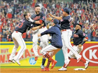  ?? Phil Long / Associated Press ?? Indians catcher Yan Gomes (second from left) is hugged by pitcher Josh Tomlin and mobbed by teammates after hitting a game-winning single in the 13th inning to beat the Yankees in Game 2.