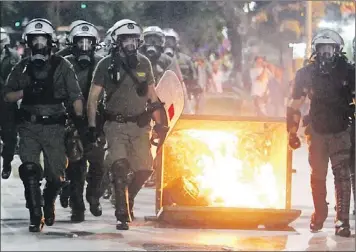  ?? — Photo by The Associated Press ?? Riot police walk past a burning garbage bin during a protest in Thessaloni­ki, Greece, Wednesday.