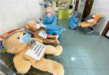  ?? — ZaInudIn aHad/The star ?? Bear care: nurses siti nursyafiqk­a shamsuri (left), 20, and nur Ismaniza Ismail, 26, sanitising the teddy bears wearing face masks and shields that are placed on chairs to ensure social distancing at a dental clinic in Bayan Baru, Penang.