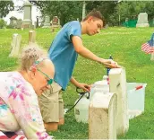  ?? ?? Madonna White and Aaron Schultz plant American flags near each cleaned headstone.