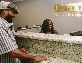  ?? Dave Rossman ?? Jesse Lamb is helped at the counter by teller Earleisha Ryan at the Unity National Bank on Blodgett. Unity National is the only African-American-owned bank in Texas.