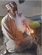  ??  ?? A Pakistani man smoking hashish in a chillum pipe near a shrine in Peshawar.
