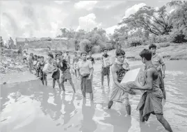  ?? ASSOCIATED PRESS ?? Rohingya Muslims carry food items across from Bangladesh towards no man's land where they have set up a refugee camp, as smoke rise from fire across the border in Myanmar, in Tombru.