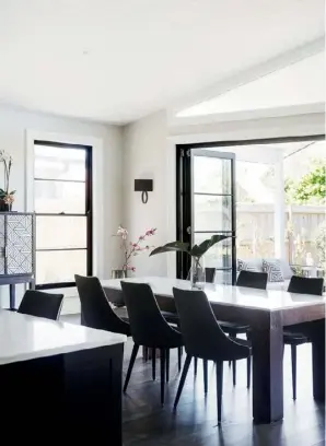  ??  ?? DINING ROOM Black steel doors and windows from Trend Windows &amp; Doors add drama when paired with walls in Dulux Brume (top &amp; above). “I wanted it to have a really classic feel and not to feel too modern,” says Therese. The monochrome look is continued with black ‘Markson’ dining chairs with white piping, sourced from Coco Republic – “I love the formality of the piping,” says Therese – and a kitchen island topped with Carrara marble. The herringbon­e-patterned ‘Bone Inlaid’ bar cabinet from West Elm (above) has a New York vibe about it and is topped with a vintage green vase, found by Derek’s father, Brian.