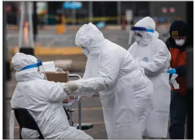  ?? (Chicago Sun-Times/Pat Nabong) ?? Medical workers help each other with their suits on Sunday at a drive-thru testing site in the parking lot of a Walmart store in
Northlake, Ill.