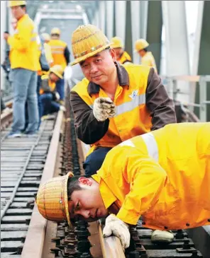  ?? DONG WEIGUO / FOR CHINA DAILY ?? Zhang Xinchao (top), 50, checks the rails with colleagues on a section of the Xinxiang bridge.