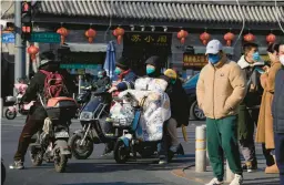  ?? NG HAN GUAN/AP ?? People wearing masks to protect against COVID-19 wait at a traffic crossing Wednesday in Beijing. China is now scaling back some of its strict anti-virus restrictio­ns.