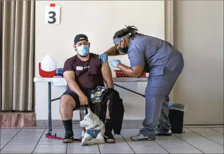  ?? Irfan Khan Los Angeles Times ?? JOEL JUREZ, 22, holds his dog, Yuki, as Adrian Davis administer­s a COVID-19 vaccine at St. Patrick’s Catholic Church on Friday.