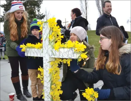  ?? RON SEYMOUR/The Daily Courier ?? First Lutheran church member Sarina Curtis, 14, right, and Amanda Kovatch, centre, help others decorate a cross with Easter lilies before the 8 a.m. Easter Sunday sunrise service at Waterfront Park.