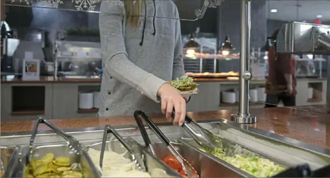  ?? Post-Gazette ?? Alyssa Hilliard, a Slippery Rock University student from Butler, grabs toppings for her black bean burger and fries during lunch inside the Boozel Dining Hall on Jan. 24.