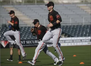  ?? AP PHOTO/ROSS D. FRANKLIN ?? San Francisco Giants catcher Buster Posey (right) jumps in the air as he warms up with teammates during spring training baseball workouts for pitchers and catchers on Wednesday in Scottsdale, Ariz.