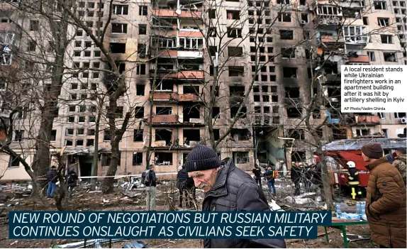  ?? AP Photo/Vadim Ghirda ?? A local resident stands while Ukrainian firefighte­rs work in an apartment building after it was hit by artillery shelling in Kyiv