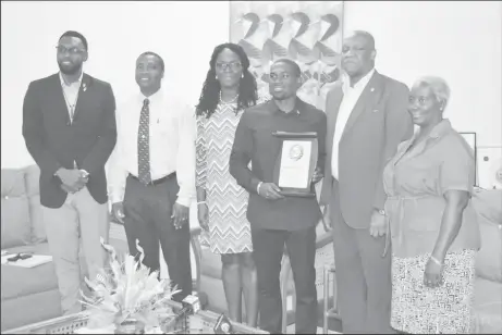  ??  ?? Troy Doris poses with his plaque of achievemen­t from Minister of State Joseph Harmon while in the presence of Director of Sports Christophe­r Jones, Permanent Secretary of the Ministry of Public Service, Reginal Brotherson (second from left) and other...