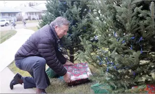  ?? NEWS PHOTO MO CRANKER ?? John Piea places a decorative present under one of St. Joe’s Trees of Light Friday afternoon. The group is accepting donations and is hoping to raise support around its programs.