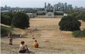  ?? ?? People sit on the sun-parched grass in Greenwich Park with the Maritime museum and Canary Wharf financial district in the background in London, Sunday July 17, 2022. Photo: AP