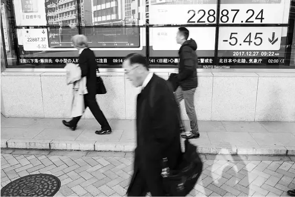  ??  ?? Passersby walk past an electronic board showing market indices outside a brokerage in Tokyo, Japan. — Reuters photo