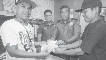  ??  ?? Erwin Cariaga (right), a maintenanc­e personnel of a mall in Lapu-Lapu City, returns the P59,000 cash he found on the escalator steps to Joel Mondares (left) who unknowingl­y dropped the cash while he was riding the escalator. The return was witnessed by police officers of Barangay Pusok police station.