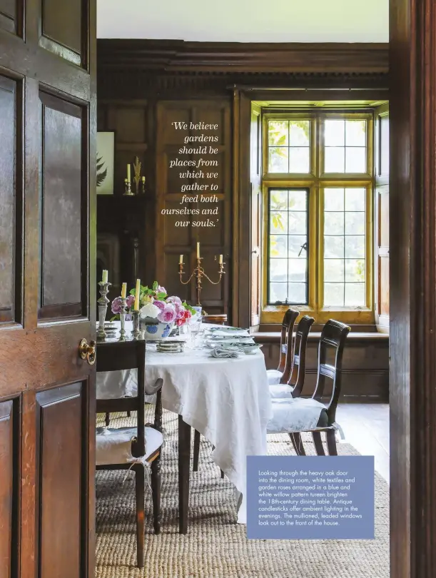  ??  ?? Looking through the heavy oak door into the dining room, white textiles and garden roses arranged in a blue and white willow pattern tureen brighten the 18th-century dining table. Antique candlestic­ks offer ambient lighting in the evenings. The mullioned, leaded windows look out to the front of the house.