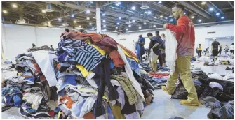  ?? AP PHOTOS ?? HOPE AND HARDSHIP: Volunteer Gene Donahue helps sort donated clothing at NRG Center, while evacuees inside the Bowers Civic Center in Port Arthur, Texas, are surrounded by floodwater­s.