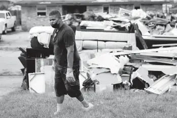  ?? GERALD HERBERT/AP ?? Derek Anthony dumps debris at the curb while gutting his LaPlace, Louisiana, home that was flooded after Hurricane Ida made landfall in late August. Storm damage has some residents debating whether to stay or move.