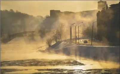  ?? (AP/Mindaugas Kulbis) ?? A car makes its way through a street along the snow-covered banks of the Neris River during sunrise as temperatur­es dipped to -5.8 degrees Fahrenheit in Vilnius, Lithuania, on Sunday.