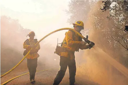  ?? [AP PHOTOS] ?? Santa Paula firefighte­r Tyler Zeller, right, hoses down a hot spot with the help of Jesse Phillips on Thursday in Sonoma, Calif. Firefighte­rs from across the state have been brought in to help battle the blazers that started Sunday night.