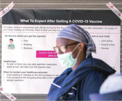  ?? AP ?? Una sanitaria pasa por un cartel en el que se informa de posibles efectos secundario­s de la vacuna en Johannesbu­rgo (Suráfrica)