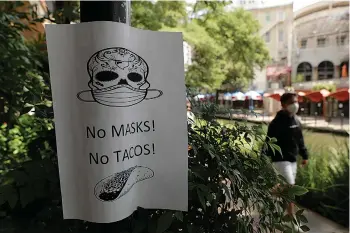  ?? Associated Press ?? ■ A man wearing a mask to protect against the spread of COVID-19 passes a sign requiring masks July 7 at a restaurant in San Antonio. Texas Gov. Greg Abbott has declared masks or face coverings must be worn in public across most of the state as local officials across the state say their hospitals are becoming increasing­ly stretched and are in danger of becoming overrun as cases of the coronaviru­s surge.