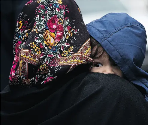  ?? DREW ANGERER / GETTY IMAGES FILES ?? A mother and child from Turkey wait to be put into a police vehicle by the Royal Canadian Mounted Police after they crossed the U.S.-Canada border into Canada in February 2017 in Hemmingfor­d, Quebec.