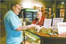  ?? STAFF PHOTOS BY TIM BARBER ?? Longtime employee Charlie Bigham, right, serves customer Chris Moffat in his cigar purchase Wednesday at Burns Tobacconis­t.