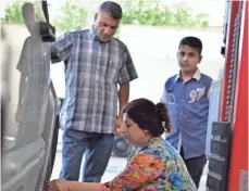  ?? HALWEST ABDULKAREE­M ?? A woman who works at the auto-repair garage checks a vehicle’s tires as a customer looks on.