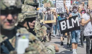  ?? Brian van der Brug Los Angeles Times ?? PROTESTERS march in Hollywood past National Guardsmen. County Supervisor Janice Hahn said that while curfews may have been warranted, “now it seems like they are being used to arrest peaceful protesters.”