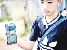  ?? — AFP photo ?? Thananchai Saengtan, 15, shows the camera photo of his missing friends, at a football pitch near Tham Luang cave.