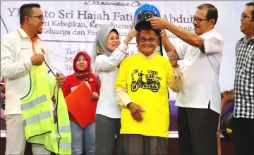  ??  ?? Fatimah and Dalat District Officer Kueh Lei Po help 83-year-old Suhaili put on the helmet. At left is JPJ Sarawak director Mohd Syafiq Anas Abdullah.