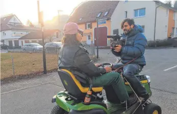  ?? FOTO: REES ?? Dreharbeit­en in Rietheim-Weilheim: Auf der Motorhaube sitzt Kameramann David Hulik, während Hauptdarst­eller Peter Hofmann auf dem Rasenmäher­traktor durch den Ort fährt.