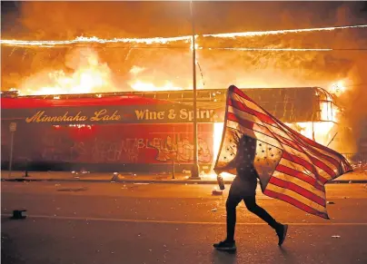  ??  ?? ANGER: A protester carries an upside-down Stars and Stripes next to a burning building in Minneapoli­s