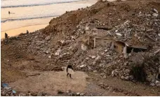  ?? AFP ?? A surfer walks past the rubble of houses that were demolished by authoritie­s in the Moroccan town of Imsouane