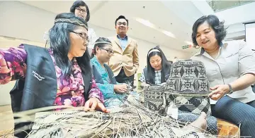  ??  ?? Aisah (right) examines one of the products created by the Murum Penan artisans after officiatin­g the new collection yesterday.Also seen here are some of the artisans attending the event – (seated from left) Bawe Adu, Tijan Paneh and Roska Asan. —...