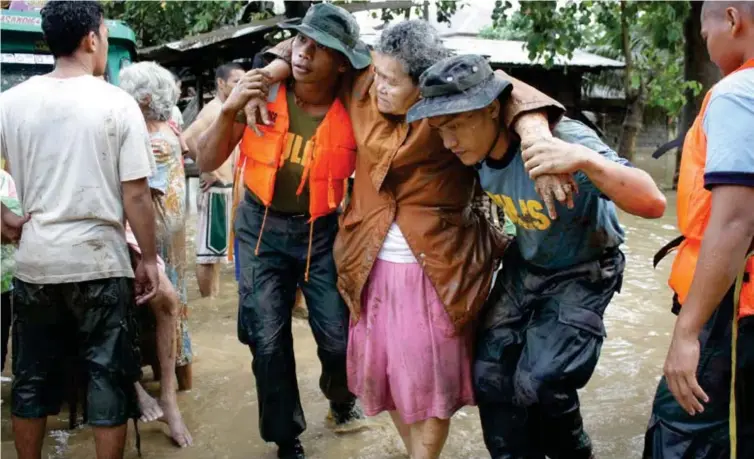  ?? (JB R. DEVEZA) ?? FILE. Policemen help carry an old woman in this photo taken at 7:50 in the morning of Saturday, December 17, 2011, along the Biasong-Tinib Road, Barangay Macasandig, Cagayan de Oro City. Parts of Macasandig village were among the worst-hit by the flash...
