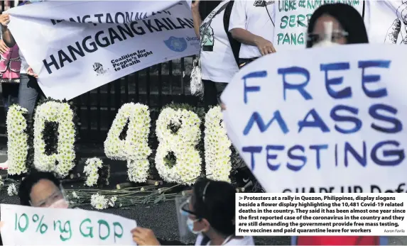  ?? Aaron Favila ?? Protesters at a rally in Quezon, Philippine­s, display slogans beside a flower display highlighti­ng the 10,481 Covid-19 related deaths in the country. They said it has been almost one year since the first reported case of the coronaviru­s in the country and they are still demanding the government provide free mass testing, free vaccines and paid quarantine leave for workers