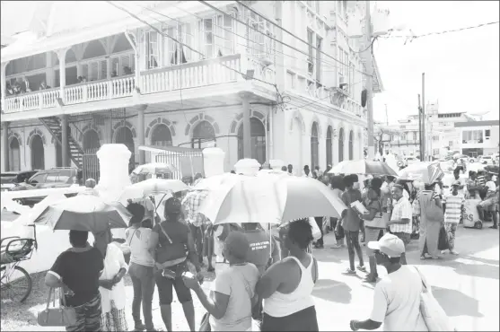  ??  ?? Demonstrat­ors and some curious onlookers outside the courthouse yesterday. Many braved the sweltering afternoon sun, while others used their umbrellas.