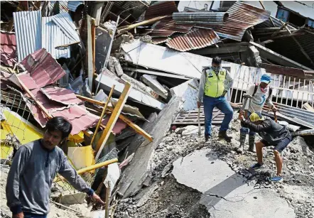  ?? — AP ?? Down to basic tools: Men using hammers and shovels to try to recover the bodies of their relatives buried under the rubble of their house in Palu.